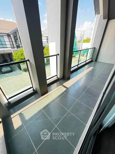 Spacious balcony with modern glass railing and scenic view of residential area.