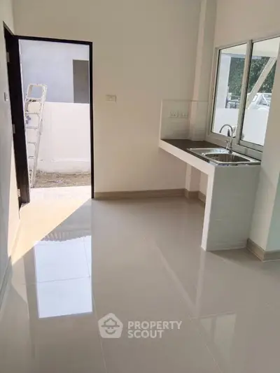 Bright kitchen with sleek tile flooring and modern sink, opening to a sunny outdoor area.