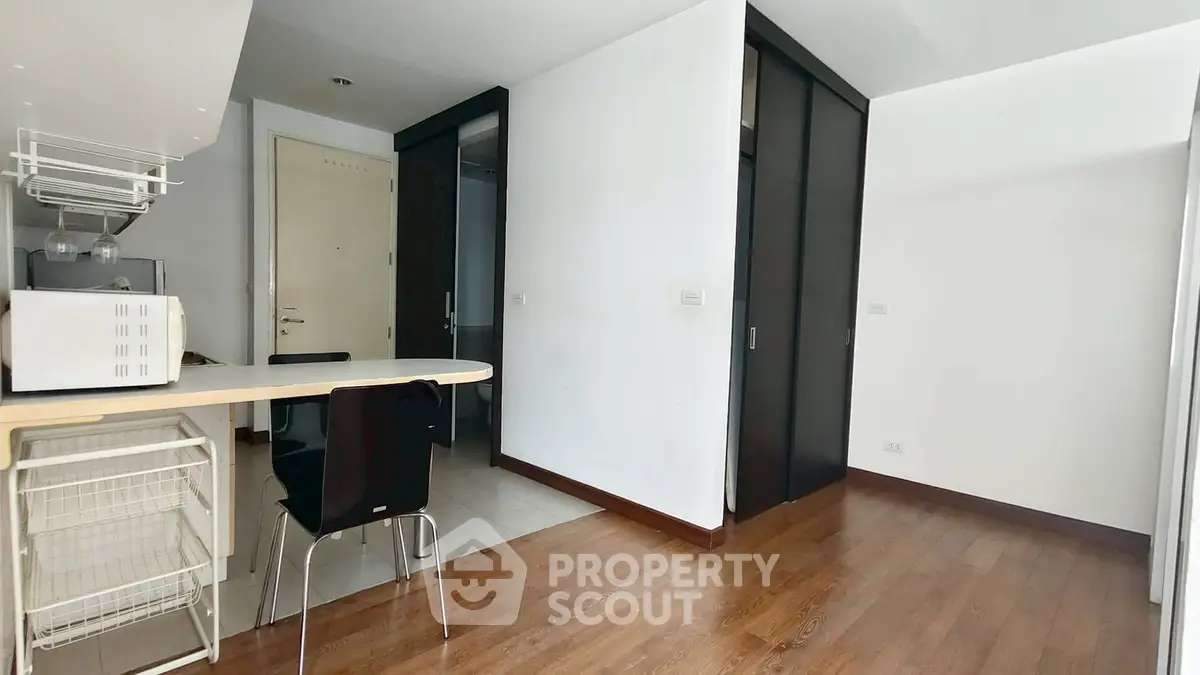Modern apartment interior with sleek kitchen and dining area, featuring wooden flooring and minimalist design.