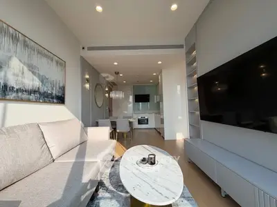 Modern living room with sleek furniture and open kitchen layout, featuring large TV and stylish decor.