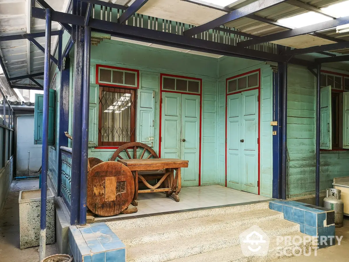 Charming vintage porch with teal wooden walls, dual entry doors, and a rustic wooden cart adding a touch of historical appeal.