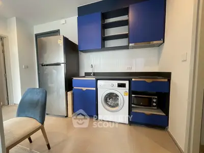 Modern kitchen with blue cabinets, washing machine, and stainless steel fridge in compact layout.
