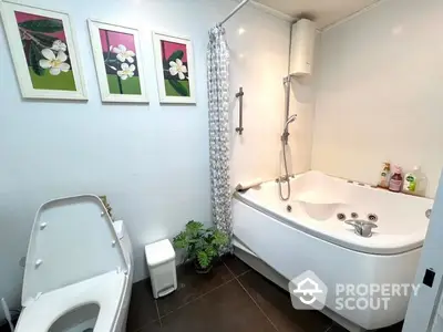 Spacious modern bathroom with a large jacuzzi tub, separate shower area, and elegant dark floor tiles, complemented by vibrant floral wall art.