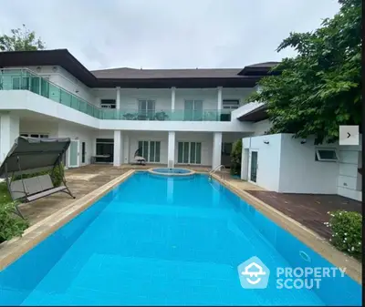 Luxurious white villa with a sparkling blue swimming pool, surrounded by lush greenery and a spacious poolside area for relaxation and entertainment.