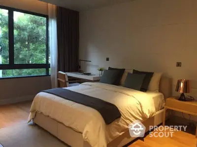 Serene bedroom with large window offering a lush green view, complemented by warm lighting and modern furnishings for a tranquil living experience.