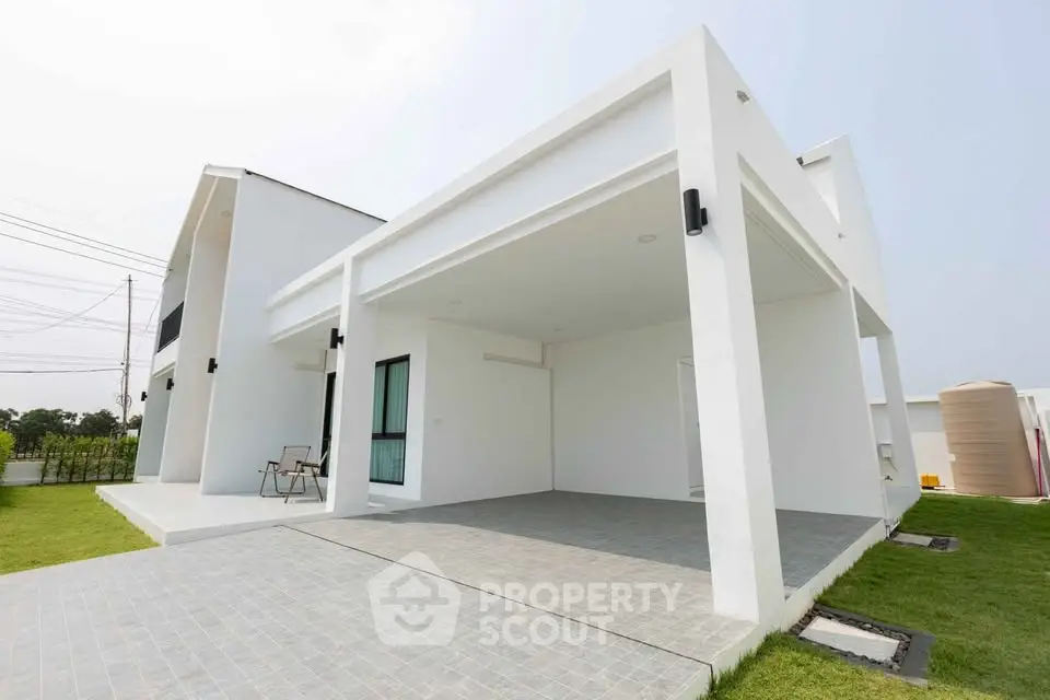 Modern minimalist white house exterior with spacious driveway and lush green lawn.