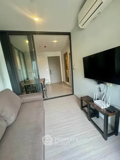 Modern living room with sleek design, featuring a comfortable sofa, wall-mounted TV, and air conditioning.