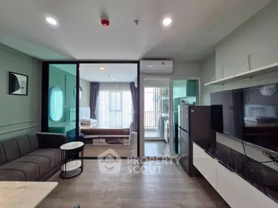 Modern open-plan living room with sleek furniture and glass partition leading to a bright bedroom.