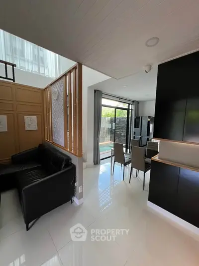 Modern open-plan living and dining area with sleek black furniture and large windows overlooking a pool.