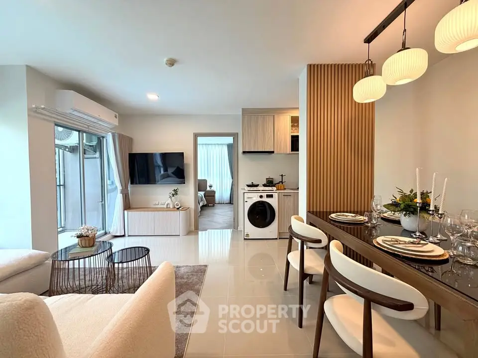 Modern open-plan living room with dining area and washing machine, featuring elegant decor and ample natural light.