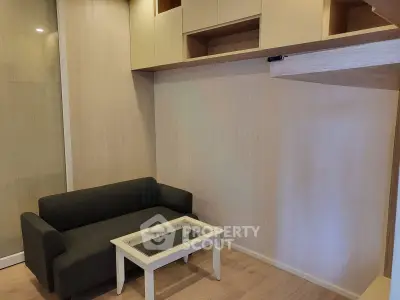 Modern living room with sleek black sofa and glass-top coffee table, featuring built-in storage cabinets.