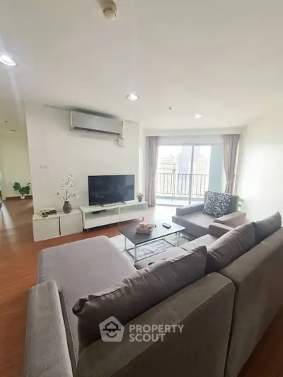 Spacious living room with modern gray sofa and city view balcony in high-rise apartment.