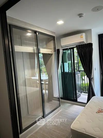 Modern bedroom with glass wardrobe and balcony access, featuring sleek design and natural light.