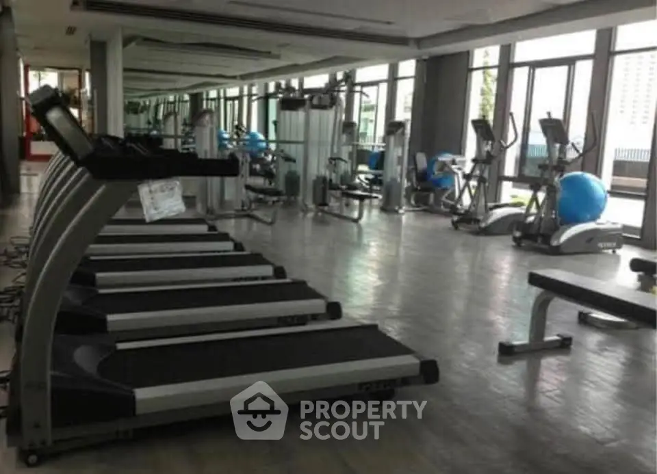 Spacious modern gym with state-of-the-art equipment and large windows offering natural light.