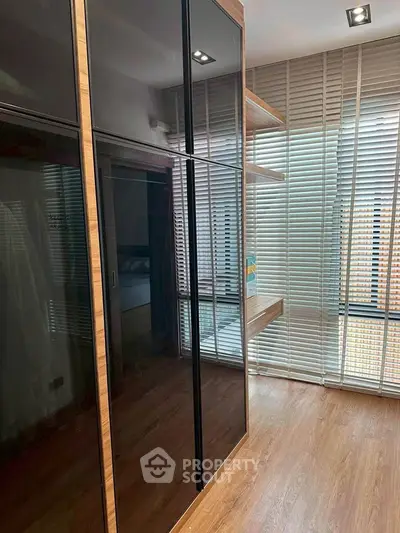 Modern bedroom with sleek wooden flooring and large mirrored wardrobe, featuring natural light through blinds.