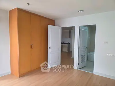Spacious bedroom with wooden wardrobe and en-suite bathroom in modern apartment.