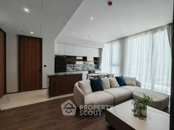Modern living room with open kitchen, featuring elegant decor and large windows for natural light.