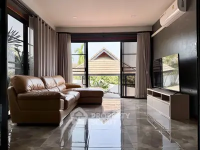 Spacious living room with modern leather sofa and large TV, featuring floor-to-ceiling windows and garden view.