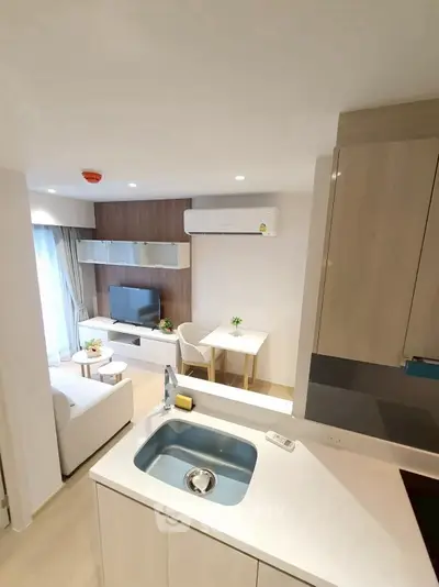 Modern open-layout living room with kitchen and dining area, featuring sleek furniture and natural light.