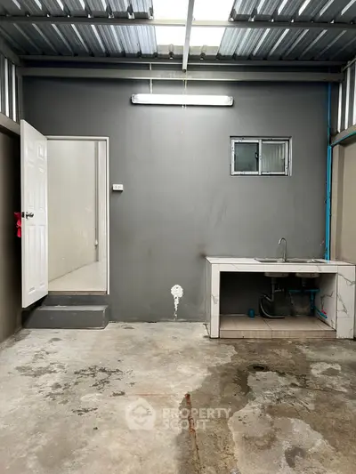 Industrial-style utility room with concrete floor and sink, ideal for storage or workshop space.