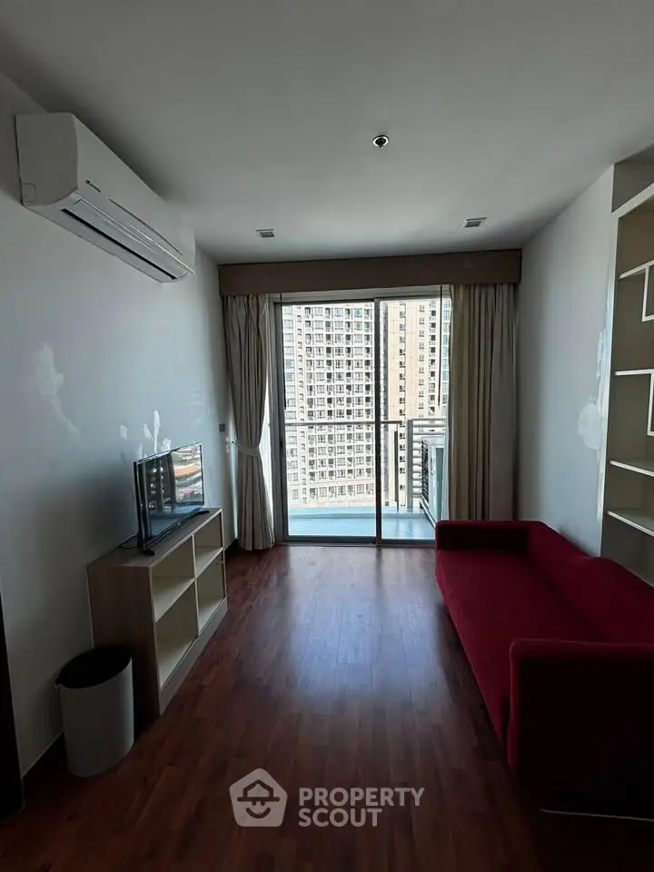 Modern living room with red sofa and city view balcony in high-rise apartment.