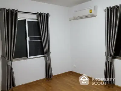 Spacious and well-lit bedroom with elegant grey curtains and air conditioning, perfect for comfortable living.