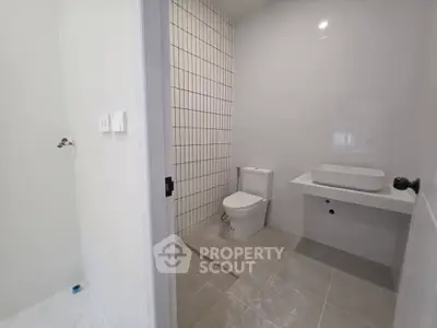 Modern bathroom with sleek design featuring a white toilet, wall-mounted sink, and tiled shower area.