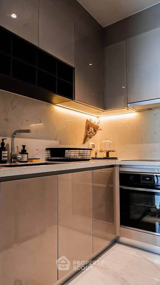 Modern kitchen with sleek cabinetry and built-in oven, featuring under-cabinet lighting and elegant decor.