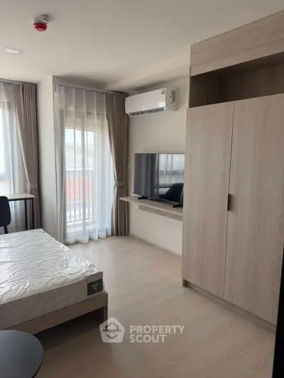 Modern bedroom with natural light, featuring a sleek wardrobe and wall-mounted TV for a cozy living experience.