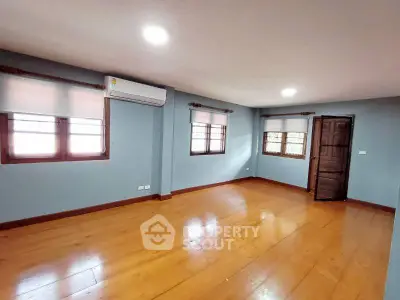 Spacious empty room with wooden flooring and large windows, perfect for customization.