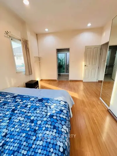 Spacious bedroom with wooden flooring and large window for natural light.