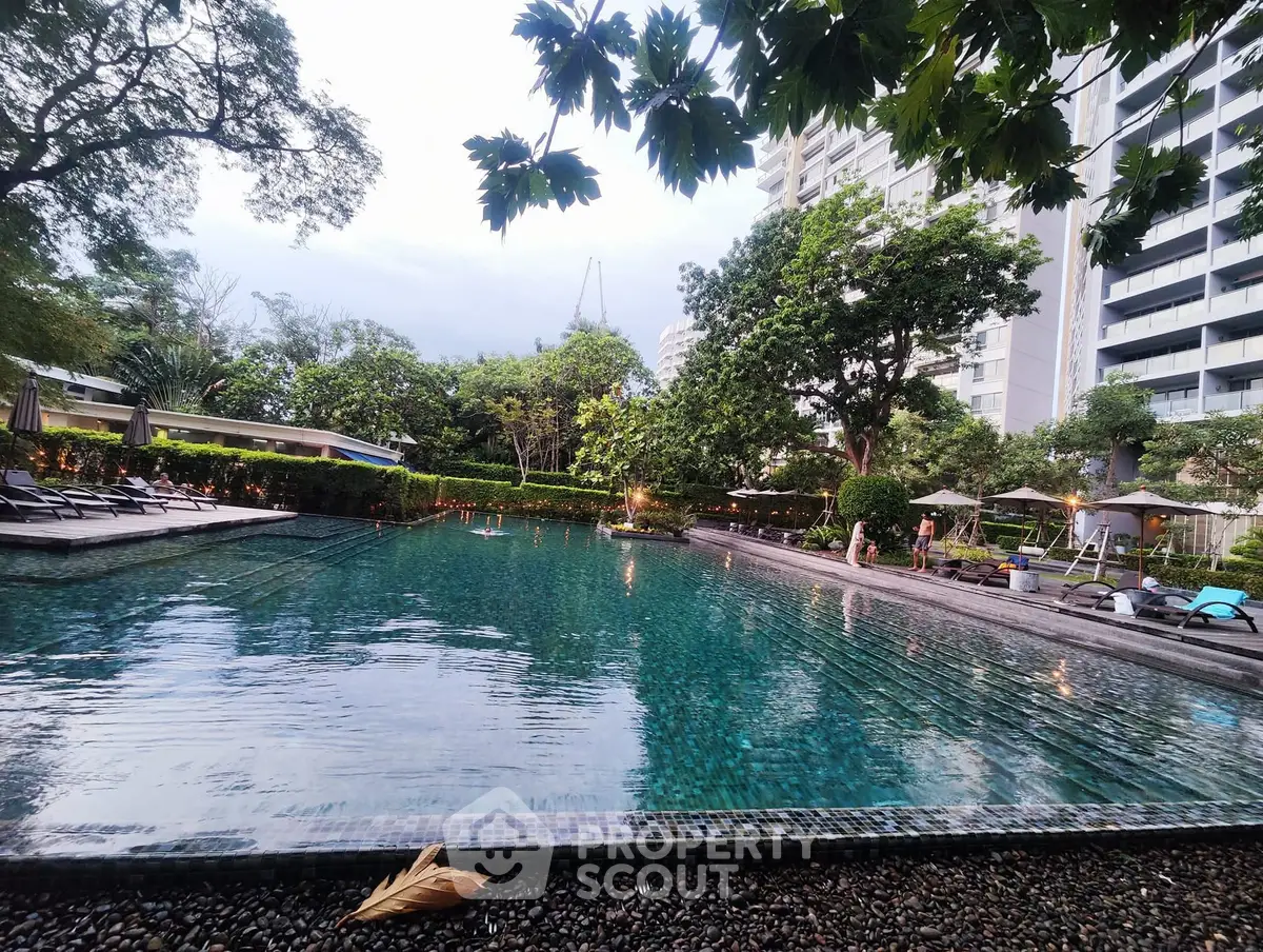Luxurious residential pool area with lush greenery and modern high-rise buildings.