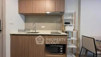Modern compact kitchen with wooden cabinets, built-in microwave, and sleek countertop in a cozy apartment.