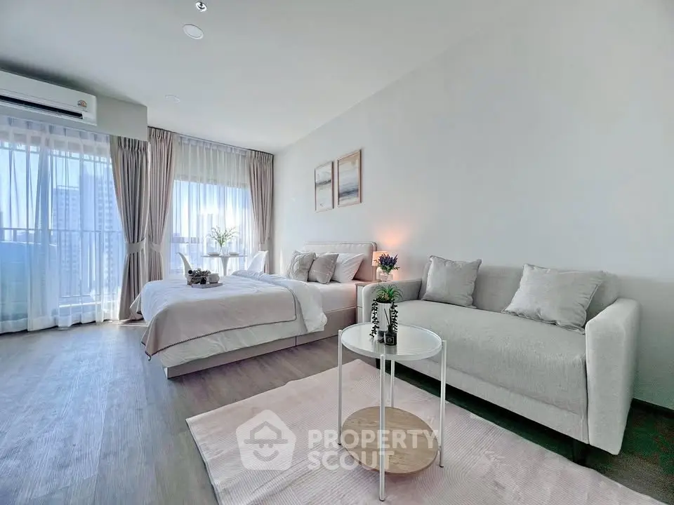 Modern studio apartment with cozy living area and large windows offering city views.
