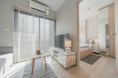 Modern living room with natural light, sleek furniture, and a view into a cozy bedroom.