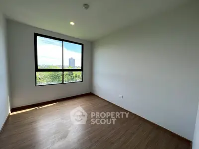 Spacious empty room with large window and wooden flooring, perfect for customization.