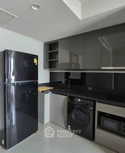Modern kitchen with sleek black appliances and glossy cabinets, featuring a fridge, washing machine, and microwave.