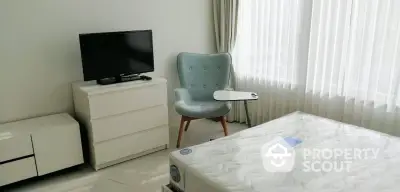 Modern bedroom with a large bed, stylish chair, and TV set, complemented by natural light filtering through sheer curtains.