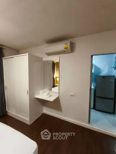 Modern bedroom with air conditioning and wardrobe, adjacent to a kitchen area with a fridge.