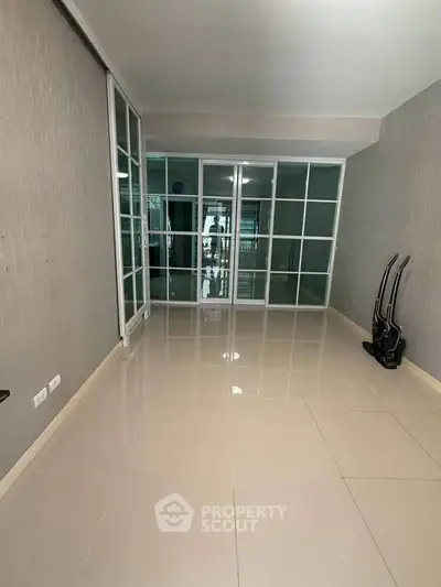 Spacious room with glossy tiled floors and glass sliding doors, perfect for versatile living space.