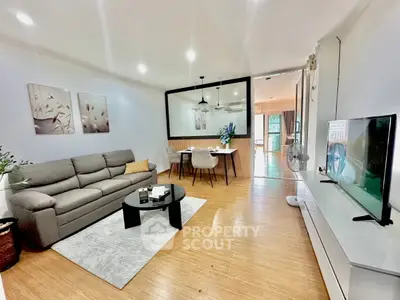 Modern living room with stylish decor and open dining area, featuring a comfortable sofa and sleek TV setup.