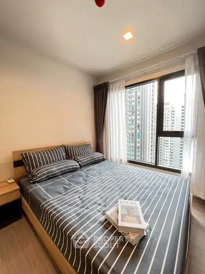 Modern bedroom with city view, featuring stylish striped bedding and large windows for natural light.