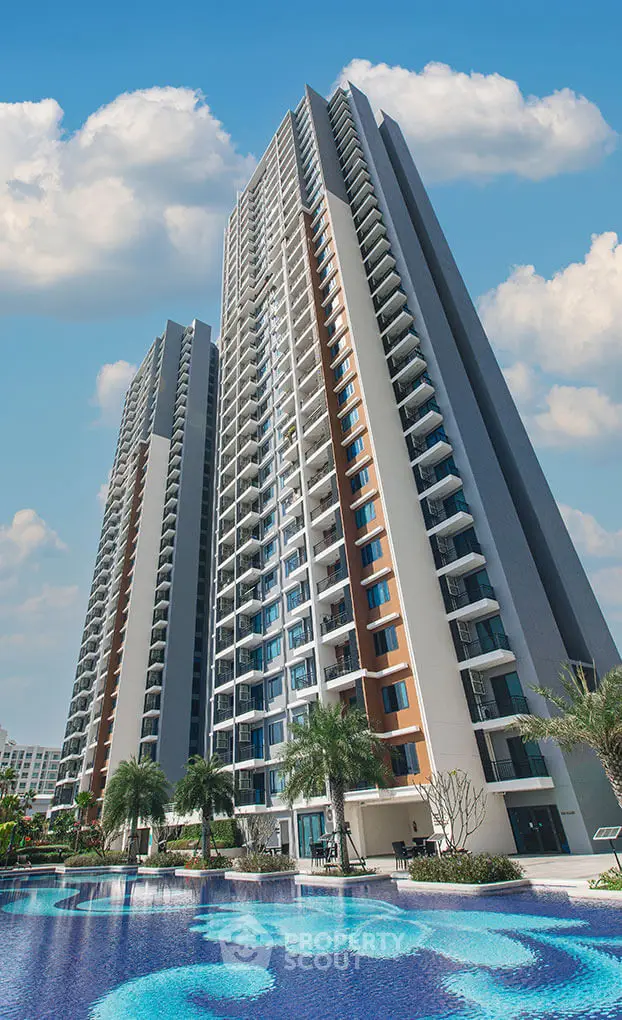 Stunning high-rise residential building with pool and lush landscaping under a bright blue sky.