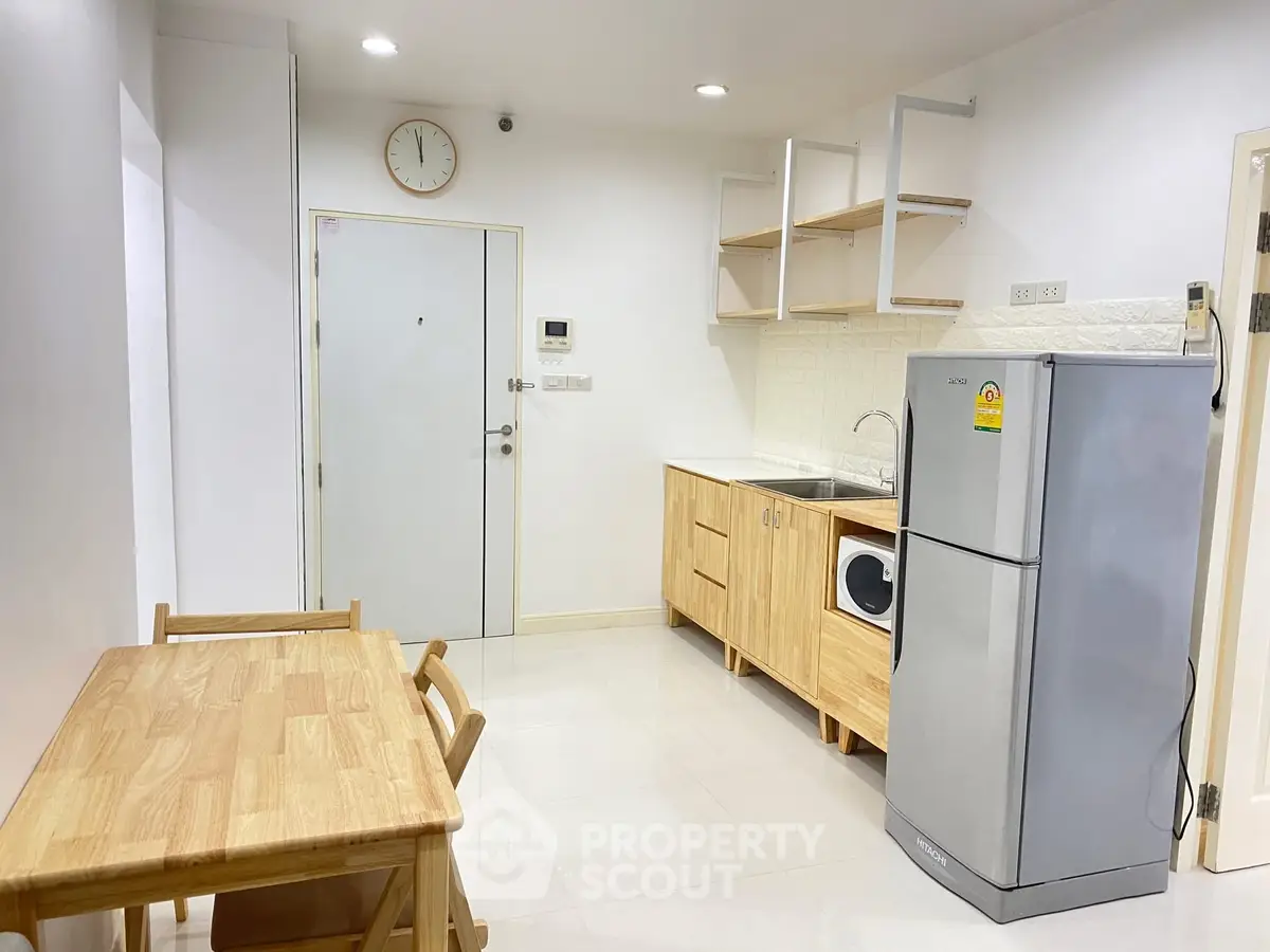 Modern kitchen with wooden cabinets, dining table, and stainless steel fridge in a compact apartment.