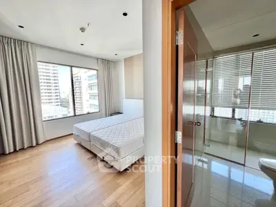 Spacious bedroom with large window and adjacent modern bathroom in city apartment.