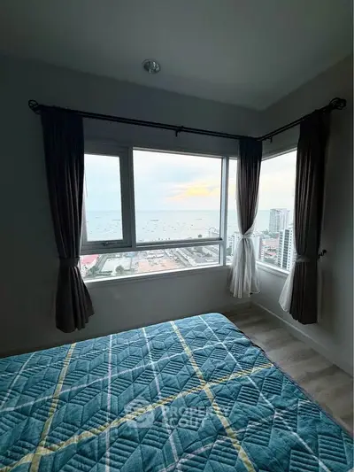 Cozy bedroom with stunning ocean view from large corner windows, featuring elegant curtains and modern decor.