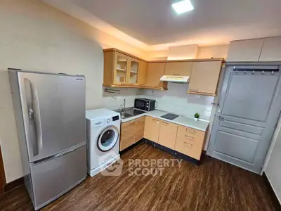 Modern kitchen with wooden cabinets, washing machine, and stainless steel fridge in cozy apartment.