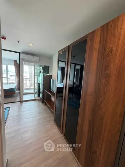 Modern apartment interior with wooden flooring and sleek wardrobe, featuring a glimpse of a cozy bedroom and balcony.
