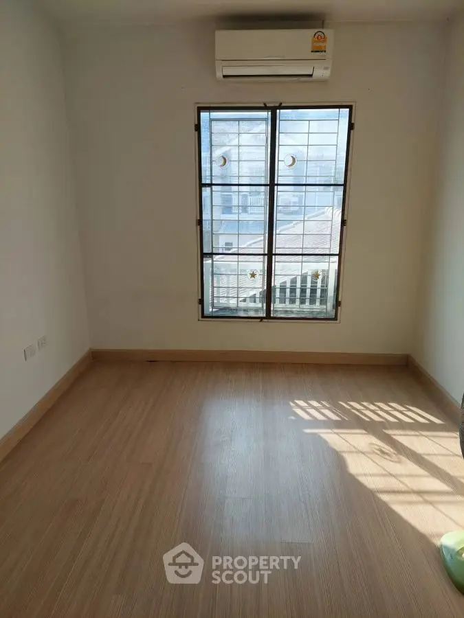 Bright empty room with wooden flooring and large window, ideal for customization.