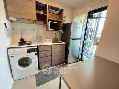 Modern compact kitchen with washing machine and stainless steel appliances in cozy apartment.